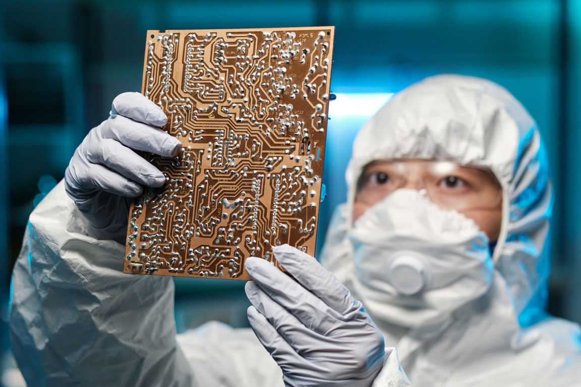 gloved-female-specialist-in-protective-coveralls man holding up semiconductor chips in hazmat suit